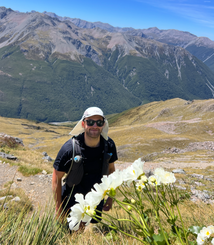 Matt standing among hills and flowers with sunglasses and a hat on.